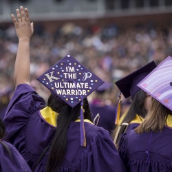 Graduates in purple at graduation, view of their hats, one that says "I am a Warrior"