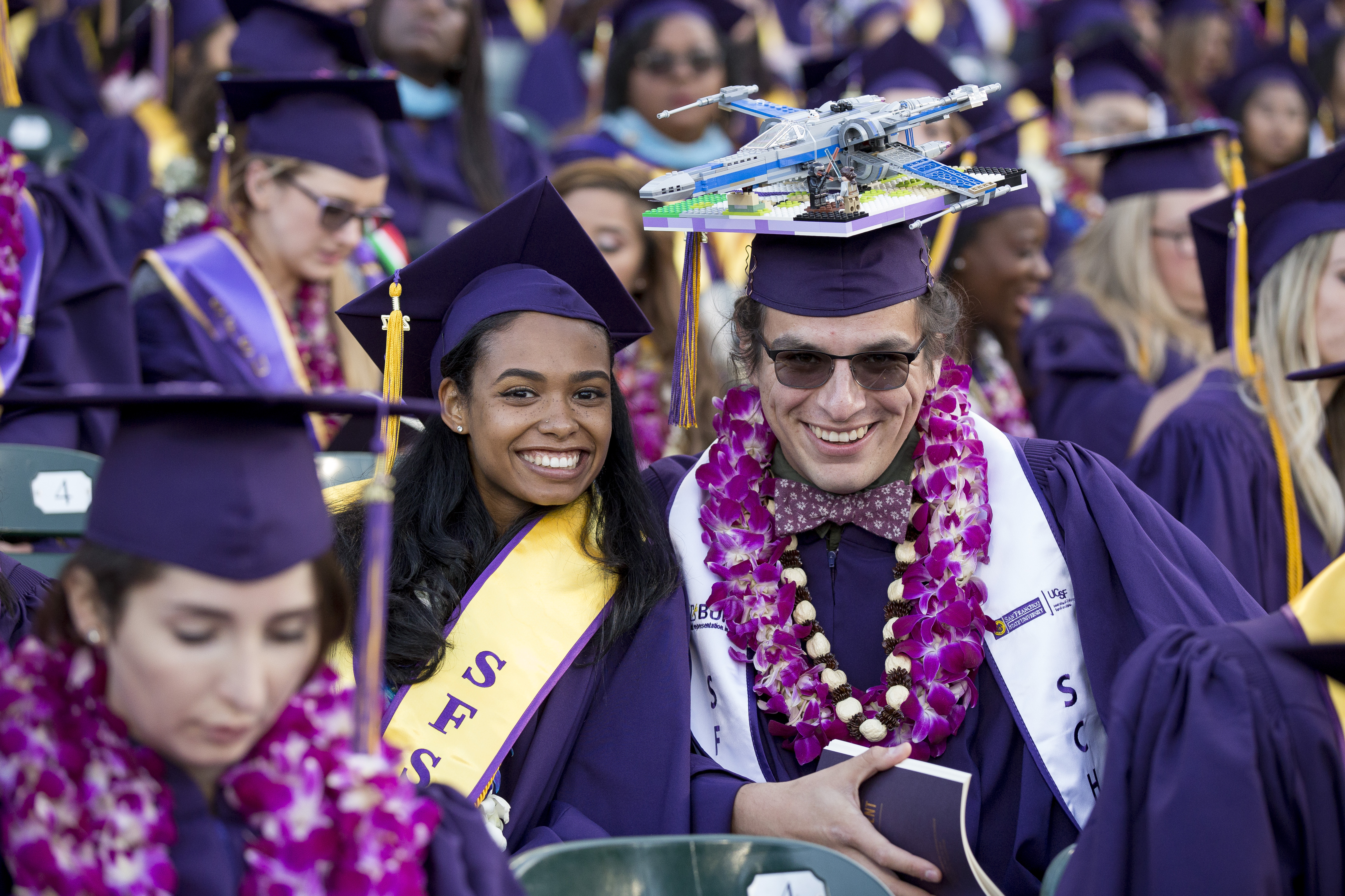 SF State graduates in cap and gown sitting and smiling