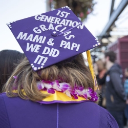 Cap and gown graduate with cap saying "1st Generation, Gracias Mami and Pai, We did it!"